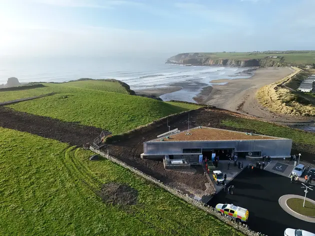 Aerial view of a coastal operations building near a beach, with vehicles and personnel visible outside